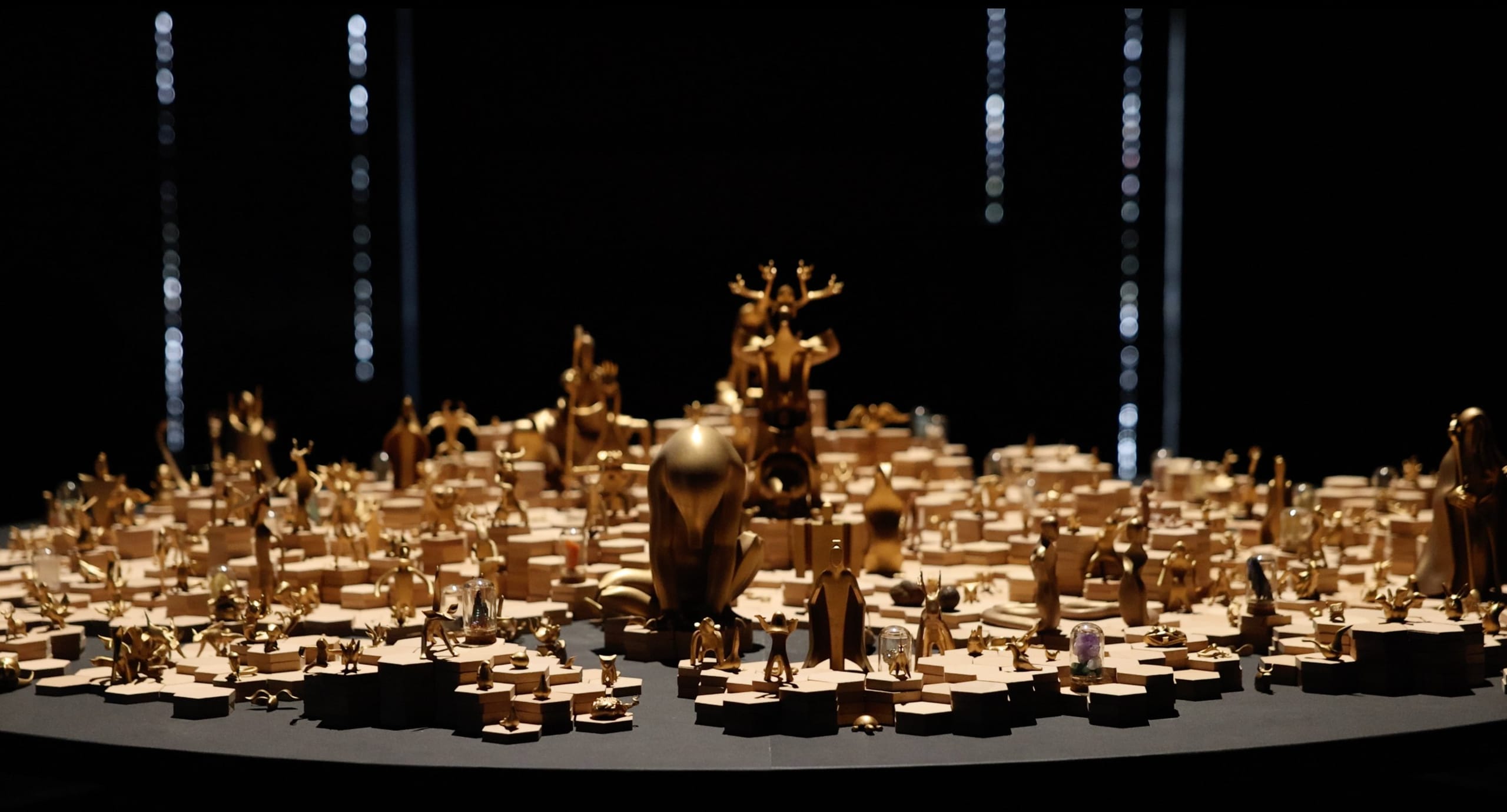 Shanhai World — gold-finished figures on a sand table under raking light