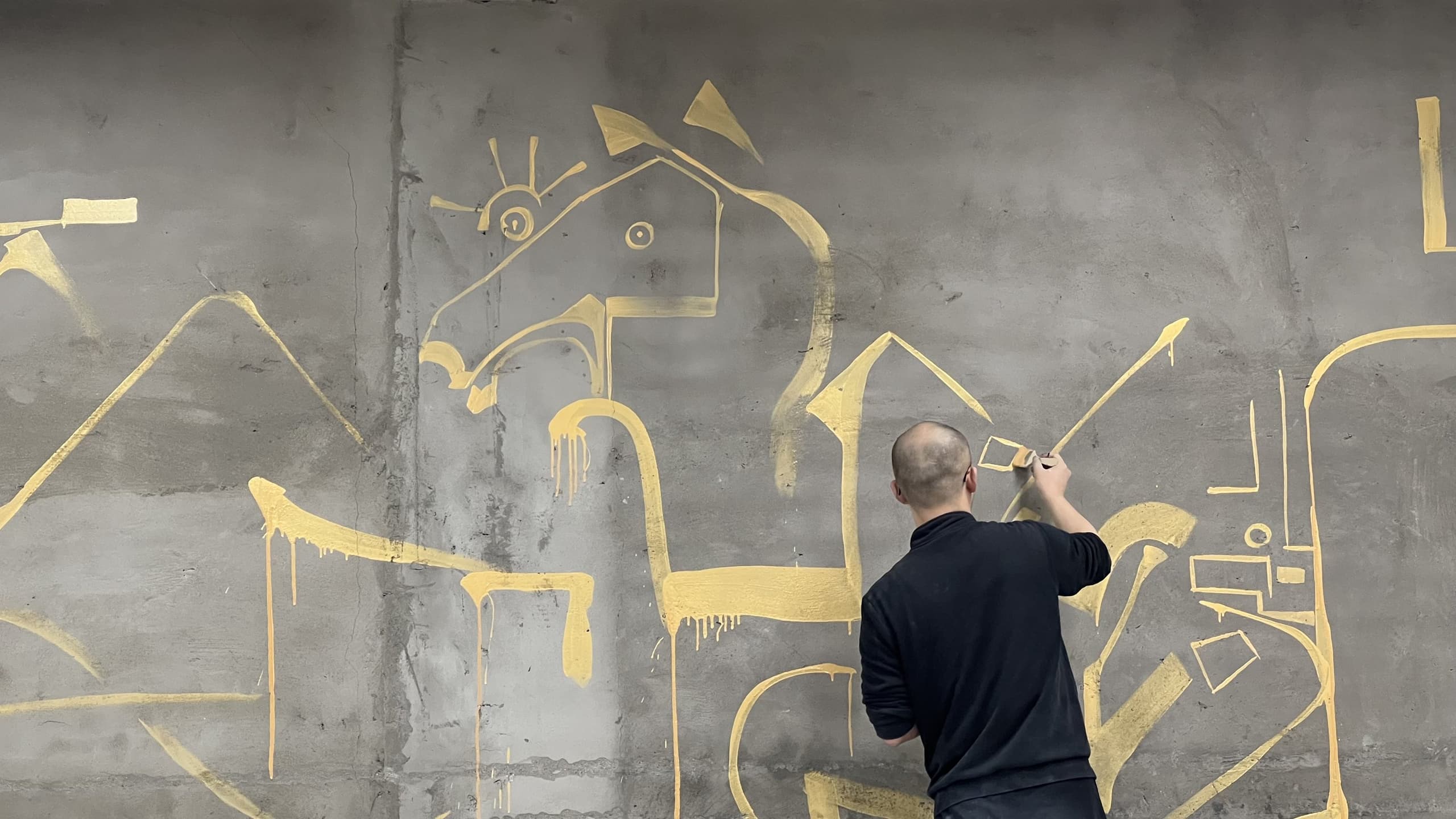 Lu Renjie painting bronze-script figures in gold on a raw concrete wall